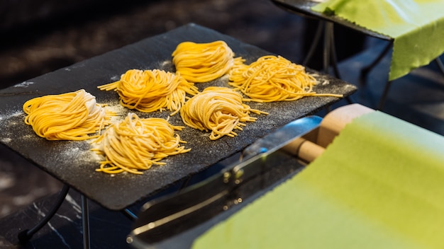 Zelfgemaakte stapels verse pasta van eierspaghetti die bloem verpoederen om te voorkomen dat ze blijven plakken