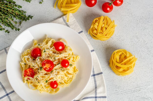 Zelfgemaakte tagliatelle pasta met tomaten, tijm, parmezaanse kaas in een witte plaat