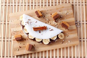 Zelfgemaakte tapioca of beiju gevuld met banaan en chocolade op witte plaat over rustieke houten tafel
