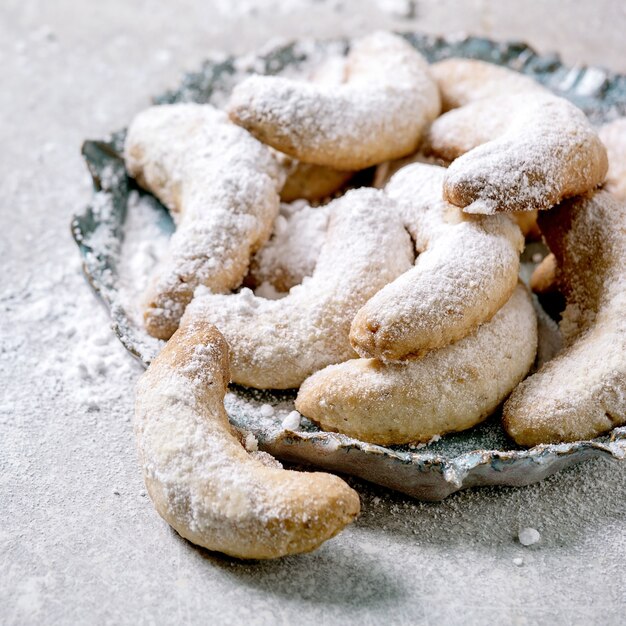 Zelfgemaakte traditionele kerstkoekjes vanille halve maantjes met poedersuiker. Op keramische plaat over lichtgrijze achtergrond. Detailopname