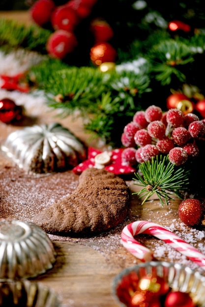 Zelfgemaakte traditionele kerstkoekjes zandkoek chocolade halve manen met cacaosuikersuiker in keramische plaat met cookie mallen, dennenboom, rode xmas sterren decoraties op houten achtergrond