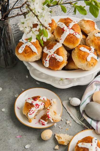 Zelfgemaakte traditionele warme kruisbroodjes van Pasen en beschilderde eieren op een grijze ondergrond