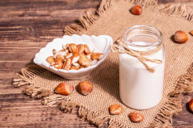 Zelfgemaakte vegan geroosterde hazelnootmelk in een glas. Niet-zuivel gezond product, oude houten tafel. Modern hard licht, donkere schaduw, kopieerruimte