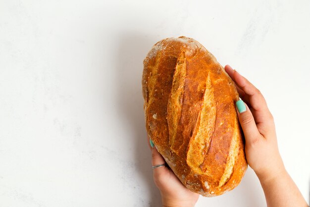 Zelfgemaakte vers gebakken natuurlijke gezond brood in handen van een vrouw op een lichtgrijze marmeren achtergrond.