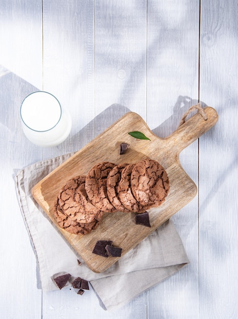 Zelfgemaakte verse chocoladekoekjes met chocoladeschilfers op snijplank en glas melk op een lichte ochtend houten tafel. Bovenaanzicht en kopieer ruimte