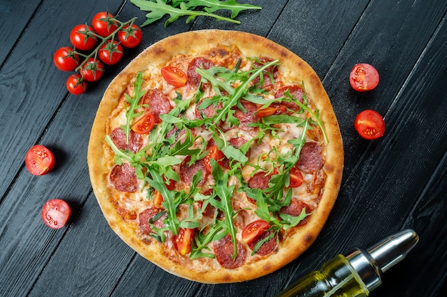 Zelfgemaakte verse pizza met salami, cherrytomaatjes en rucola op een zwarte houten met kopie ruimte. Bovenaanzicht eten foto.