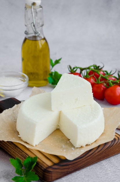 Zelfgemaakte verse zachte kaas of feta op een houten snijplank met peterselie en cherry tomaten op een grijze achtergrond.