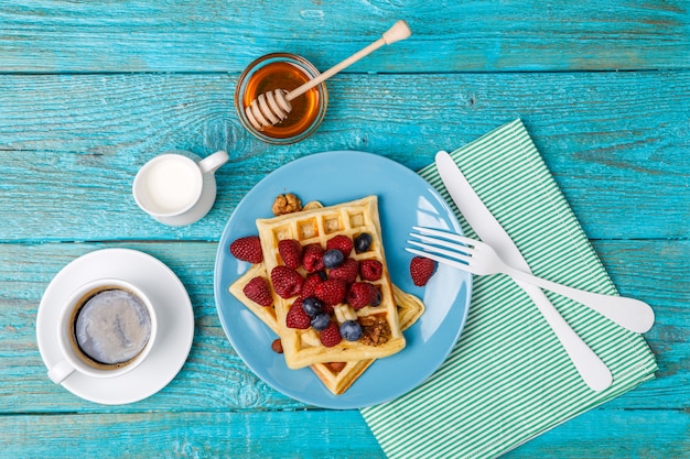 Zelfgemaakte wafels met frambozen en bosbessen, kopje koffie, melk en bestek