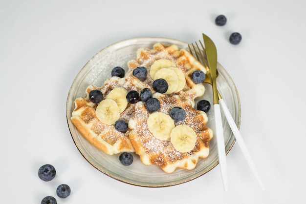 Zelfgemaakte weense wafels met bosbessen en banaan op een lichte plaat op een lichte achtergrond