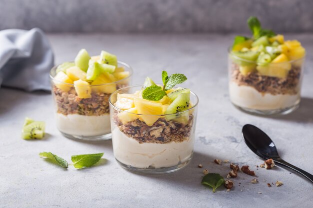 Foto zelfgemaakte yoghurt parfait met muesli, kiwi's, ananas en noten in een glas voor gezond ontbijt op concrete achtergrond