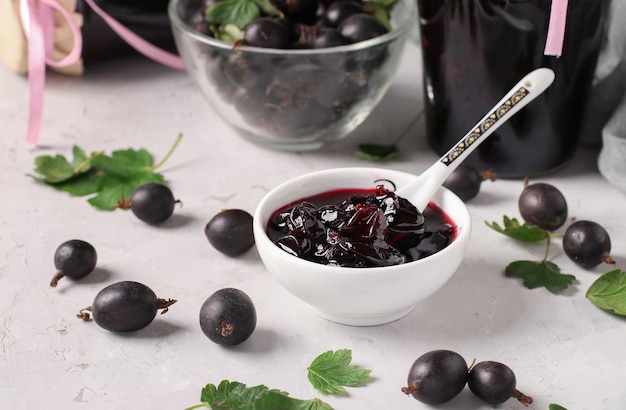 Zelfgemaakte yoshta jam met hele bessen in een kom en glazen potten op een grijze achtergrond