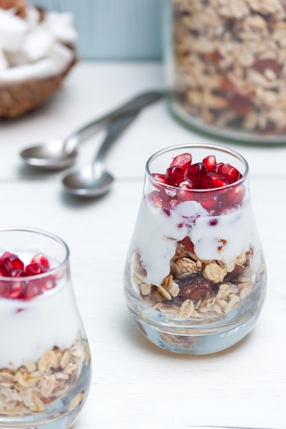 Zelfgemaakte yougurt met granola en granaatappelfruit in glazen op witte houten lijst. Gezond ontbijt.