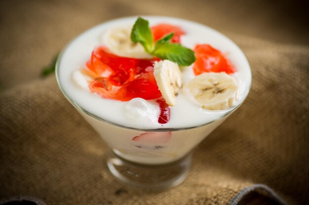 Zelfgemaakte zoete yoghurt met bananen en stukjes fruitgelei in een glas