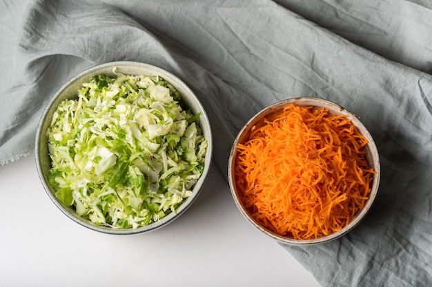 Zelfgemaakte zuurkool in een glazen pot op een grijze tafel. Snijd groene kool en wortelen voor koolsoep.