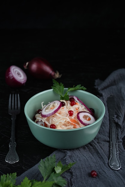 Zelfgemaakte zuurkool met wortelen met kruiden op een zwarte achtergrond. Ingemaakte kool op de plaat met zak op de houten tafel. Het concept van ingeblikt voedsel. vegetarisch eten.