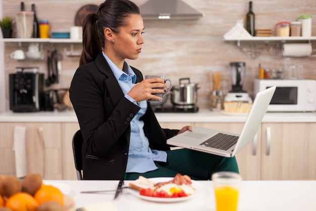 Zelfstandige die laptop gebruikt in een moderne keuken en 's ochtends een kopje koffie drinkt