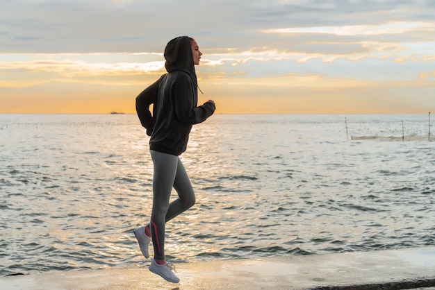 Zelfverzekerd slank meisje joggen naast de zee bij zonsondergang wil afvallen