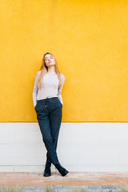 Zelfverzekerd stijlvol jong meisje model in modieuze kleding poseren tegen een gele muur achtergrond