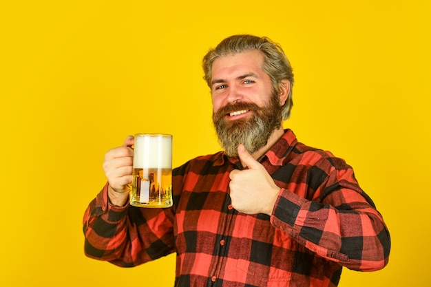 Foto zelfverzekerde barman toast op vrije tijd en feest man bier drinken in pub bar bier met schuim brutale hipster drink bier volwassen bebaarde barman houdt bierglas vast proefnotities maken