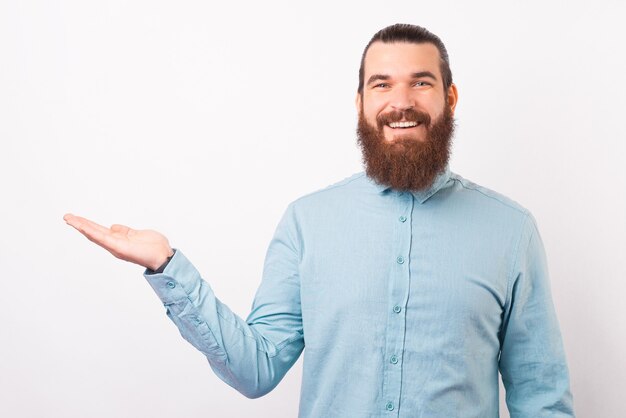 Zelfverzekerde bebaarde man met shirt presenteert je iets.