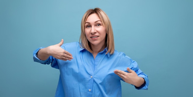 Zelfverzekerde blonde jonge millennial in casual shirt pronkt met haar look op blauwe achtergrond met kopie