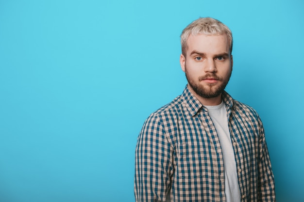 Zelfverzekerde blonde man met baard maakt reclame voor iets terwijl hij op een blauwe muur in de buurt van vrije ruimte poseert en naar de voorkant kijkt