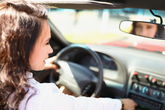Zelfverzekerde brunette vrouw zit achter het stuur van een auto en lachende vrouwelijke chauffeur kijkt