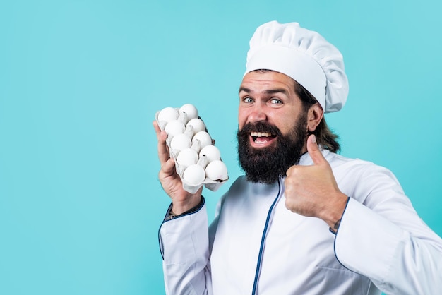 Zelfverzekerde chef-kok met baard en snor in kookuniform laat duim zien voor gezonde eieren natuurvoeding