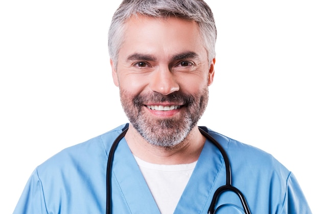 Zelfverzekerde chirurg. Portret van een gelukkige volwassen chirurg in blauw uniform die naar de camera kijkt en glimlacht terwijl hij geïsoleerd op wit staat