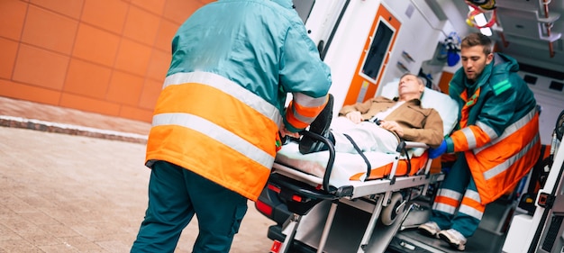 Zelfverzekerde en professionele artsen die een zieke patiënt uit een ambulanceauto lossen op een brancard in de buurt van het ziekenhuisgebouw