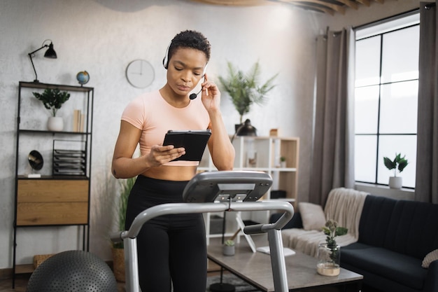 Zelfverzekerde gespierde sportieve zakenvrouw in hoofdtelefoon die op afstand van huis werkt met behulp van digitale tablet