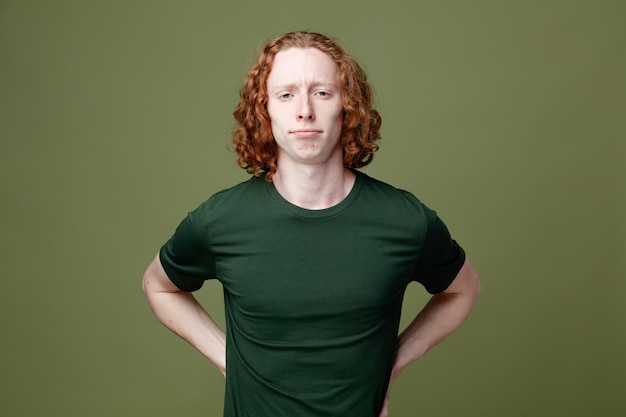 Zelfverzekerde handen op de heupen jonge knappe kerel met een groen t-shirt geïsoleerd op een groene achtergrond