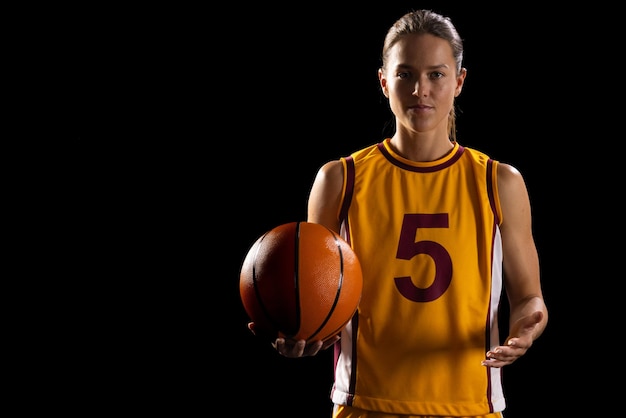 Zelfverzekerde jonge blanke vrouwelijke basketbalspeler poseert in basketbalkleding op een zwarte achtergrond