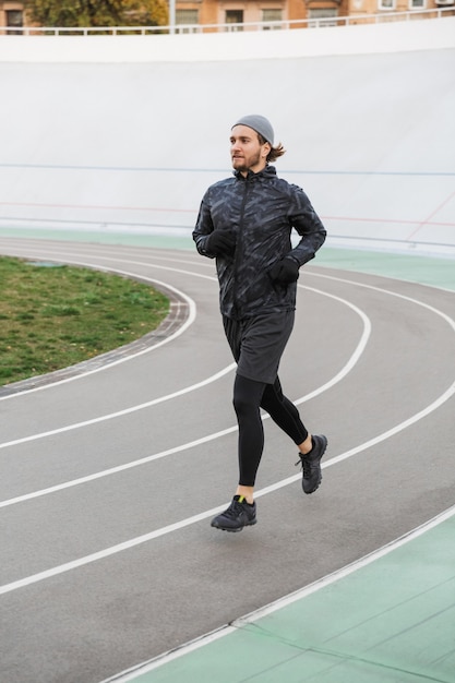 Foto zelfverzekerde jonge fitte sportman die buiten op het circuit in het stadion loopt