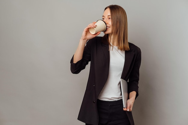 Zelfverzekerde jonge vrouw geniet van haar koffie voordat ze gaat werken terwijl ze haar laptop vasthoudt