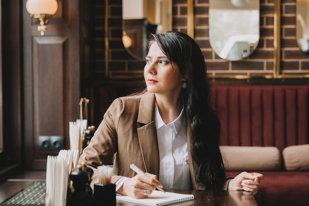 Zelfverzekerde jonge vrouw in een pak werkt op een laptop terwijl ze bij het raam zit in een cafézakenvrouw