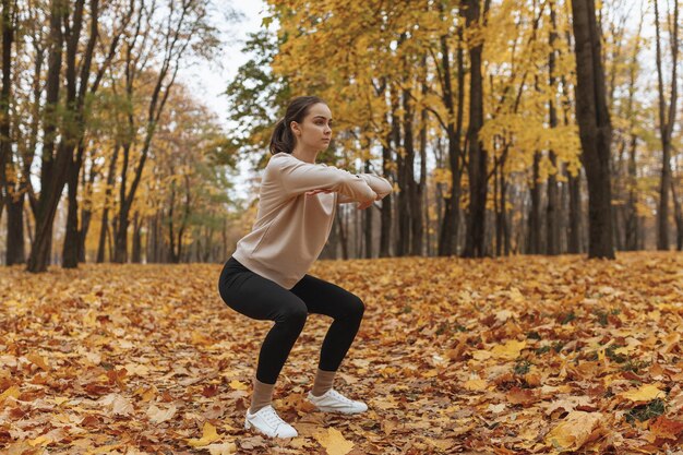 zelfverzekerde jonge vrouwelijke atleet in activewear gehurkt in herfstpark