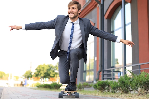 Zelfverzekerde jonge zakenman in pak op longboard haast zich naar zijn kantoor, op straat in de stad.