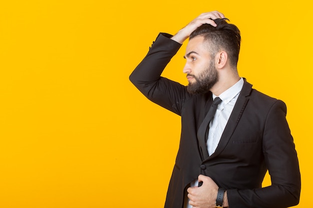 Zelfverzekerde jonge zakenman met een baard maakt zijn haar recht terwijl hij tegen een geel staat