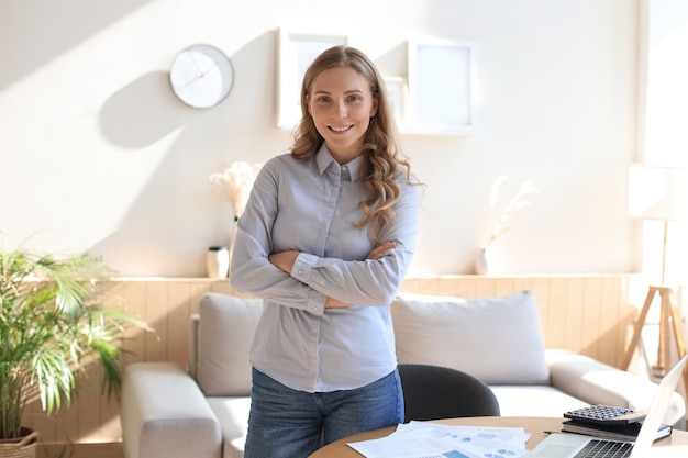 Zelfverzekerde jonge zakenvrouw met een vriendelijke glimlach achter haar bureau in een kantoor aan huis.