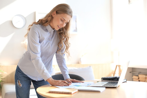 Zelfverzekerde jonge zakenvrouw met een vriendelijke glimlach achter haar bureau in een kantoor aan huis.