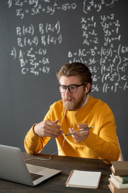 Zelfverzekerde leraar in brillen kijken naar zijn publiek op laptopvertoning tijdens het uitleggen van nieuwe formule op blackboard tijdens online les