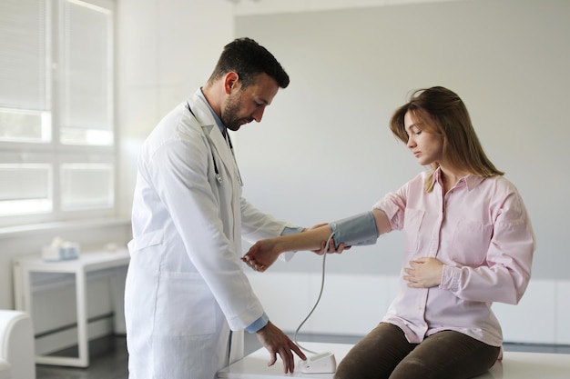 Zelfverzekerde man dokter controleert jonge zwangere vrouw hartslag en bloeddruk met behulp van tonometer