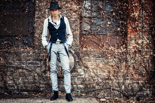 Zelfverzekerde man in fedora-stijl die met zijn handen in zijn zakken staat en naar de camera kijkt