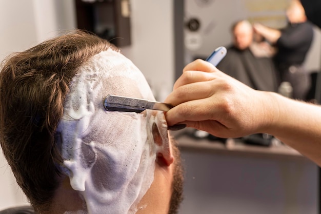 Zelfverzekerde man met brutaal blank uiterlijk die zijn baard en haar op zijn hoofd knipt gevaarlijk scheermesje scheerschuim het hoofd kaal scheren