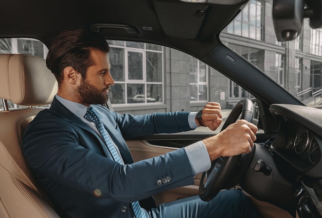 Zelfverzekerde schattige zakenman die zijn dag plant terwijl hij met de auto reist