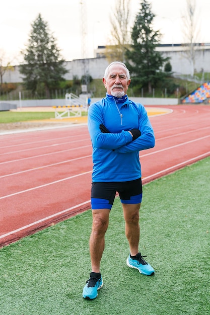 Zelfverzekerde senior hardloper in blauwe outfit die op het baanveld staat