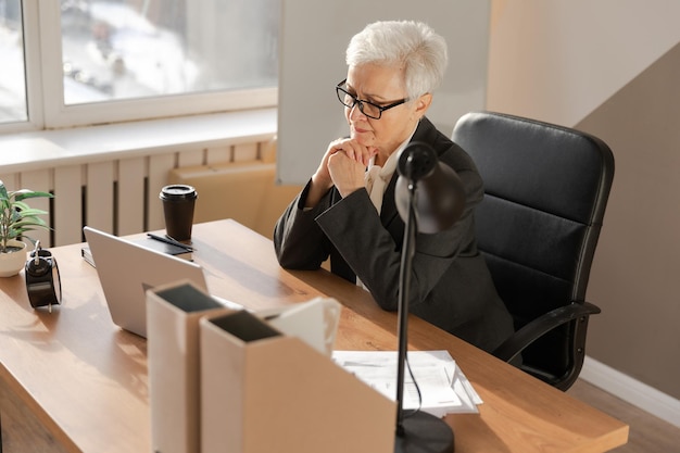 Zelfverzekerde stijlvolle Europese senior vrouw van middelbare leeftijd die laptop gebruikt op de werkplek Stijlvolle oudere volwassen 60s grijze dame zakenvrouw zittend aan kantoortafel Baas leider leraar professionele werker