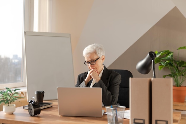 Zelfverzekerde stijlvolle Europese senior vrouw van middelbare leeftijd met behulp van laptop op de werkplek stijlvolle oudere volwassen s