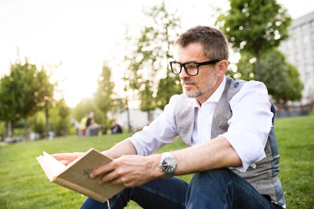 Zelfverzekerde volwassen zakenman in het stadspark zittend op gras leesboek